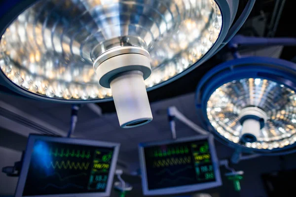 Overhead surgical light system illuminated in hospital operating theatre with patient monitors for specialist surgery by frontline doctors