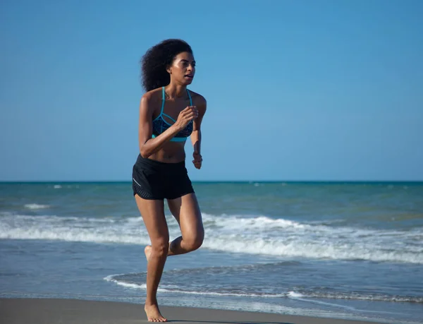 若いアフリカ系アメリカ人の女の子とビーチで海の波スポーツウェアで屋外で健康的なフィットネス活動を楽しむことによって実行 — ストック写真