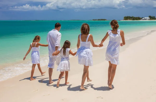 快乐健康的年轻白人家庭 身穿白衣 赤脚走在热带海滩上 沐浴在碧绿的海水中 免版税图库图片