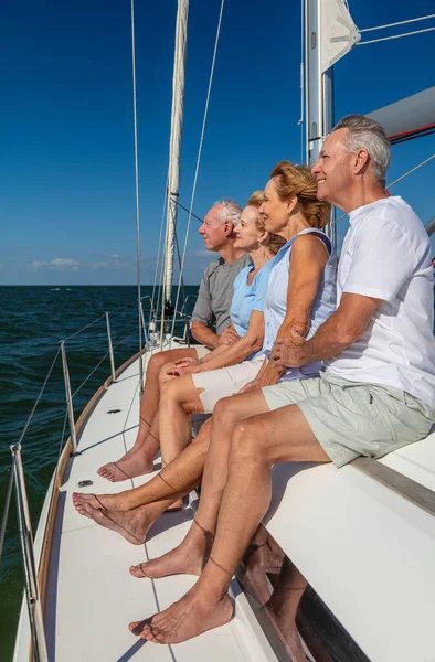 Happy group of retired friends in casual clothing relaxing together on private yacht enjoying outdoor adventures at sea