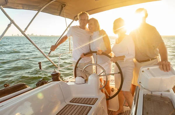Smiling group of retired friends enjoying relaxed travel on vacation steering private yacht sailing the ocean at sunrise