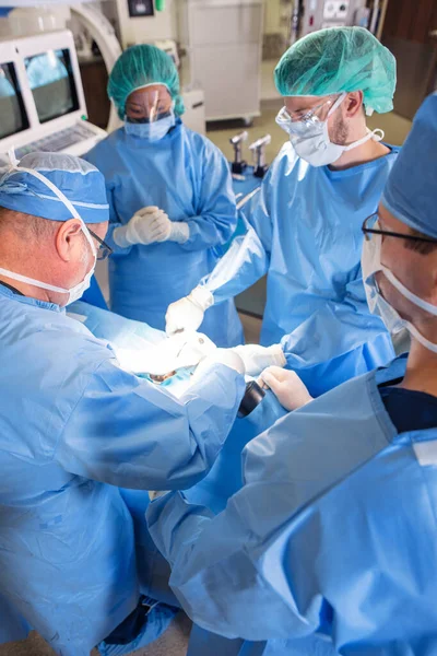 Surgical procedure on patient in operating theatre of medical training hospital with Caucasian surgeons wearing personal protective equipment