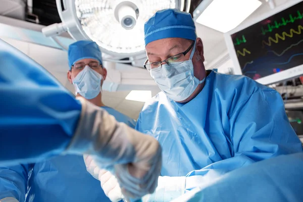 男性白人外科医身に着けています頭蓋骨と顔マスク手術で病院の劇場で患者でオーバーヘッドライト — ストック写真