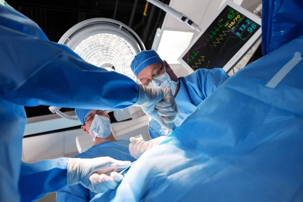 白种人男性外科医生 有医疗小组 头戴刷子 头顶灯光和病人监视器在医院手术室工作 — 图库照片