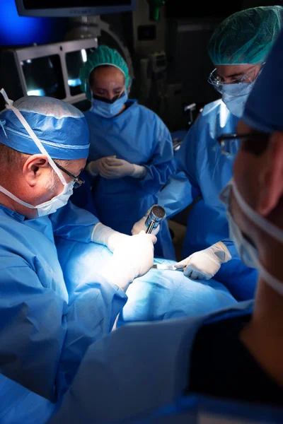 医院手术室的专家医疗队身穿个人防护装备 由白人男性外科医生对麻醉病人进行手术 — 图库照片