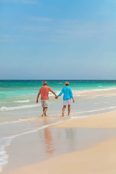 Mature Caucasian couple with active lifestyle enjoying togetherness walking through ocean on tropical island vacation holding hands Bahamas