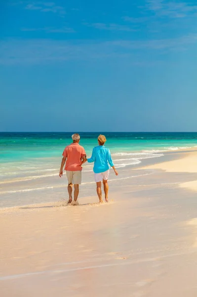 Travel senior couple enjoying romantic beach walk on tropical island vacation with blue sky and turquoise ocean Bahamas