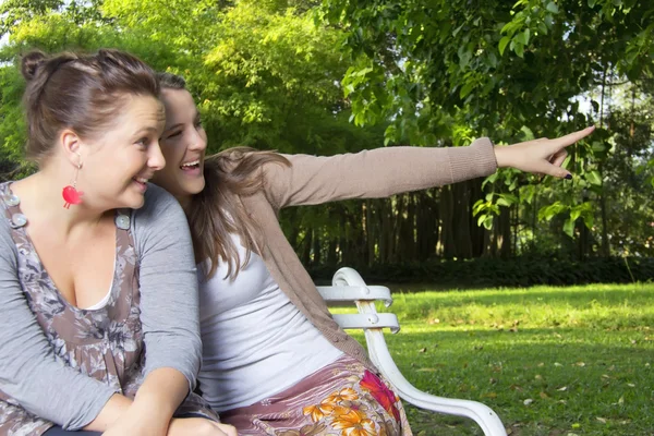 Beautiful Loving Sisters sit on a bench pointing — Stock Photo, Image