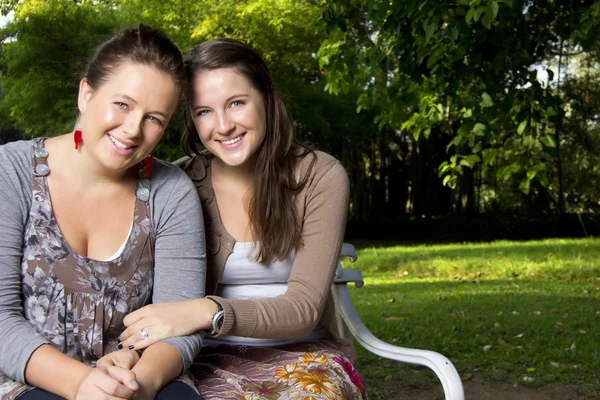 Привлекательные молодые сёстры игриво отдыхают на скамейке в парке — стоковое фото