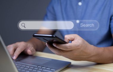 Boş bir arama çubuğuyla internette arama yap. Arama motoru optimizasyonu SEO konsepti. Akıllı telefon ve dizüstü bilgisayarla çalışan iş adamlarından oluşan eller ofis masasında..