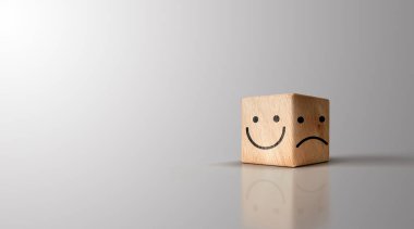Bright smiley face and dark sad face on wooden cube on gray background for positive selection idea.