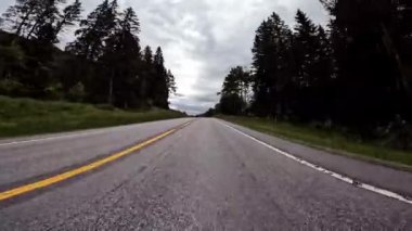 First person view of a nordic two-lane road, forest, mountains