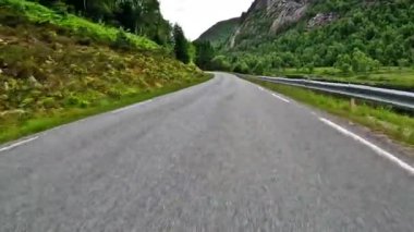 First person view of a nordic two-lane road, forest, mountains