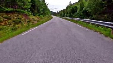 First person view of a nordic two-lane road, forest, mountains