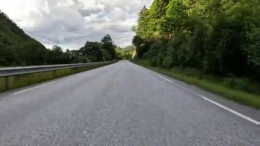 First person view of a nordic two-lane road, forest, mountains