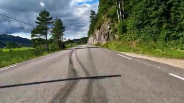 First person view of a nordic two-lane road, forest, mountains