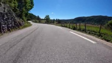 First person view of a nordic two-lane road, forest, mountains