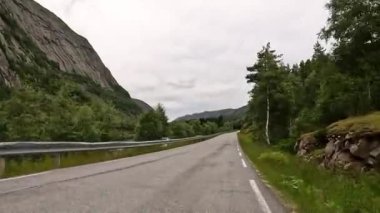 First person view of a nordic two-lane road, forest, mountains