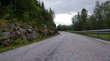 First person view of a nordic two-lane road, forest, mountains