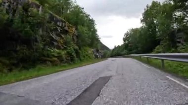 First person view of a nordic two-lane road, forest, mountains