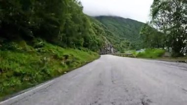 First person view of a nordic two-lane road, forest, mountains