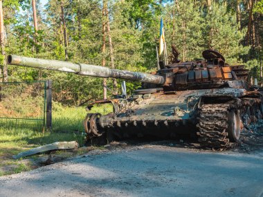 Ukrayna 'daki savaşta, yok edilmiş bir Rus tankı ormanın arka planında Ukrayna bayrağının yanında duruyor..