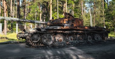 War in Ukraine, a destroyed Russian tank with a Ukrainian ensign stands near the road against the backdrop of the forest, side view