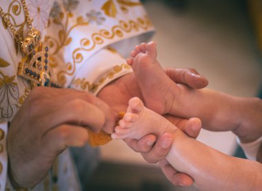 Çocuğun vaftiz töreni, kutsal baba çocuğun bacaklarını sürterek...