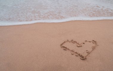 Kum yaz sahili arka planında çizilmiş aşkın kalp sembolü..