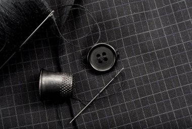 Bir iğne ve iplik ekose bir elbisenin düğmesini diker. Yüksük. Tekstil