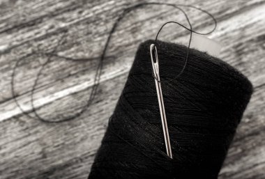 Needle with black thread. Spool of thread close up on wooden background