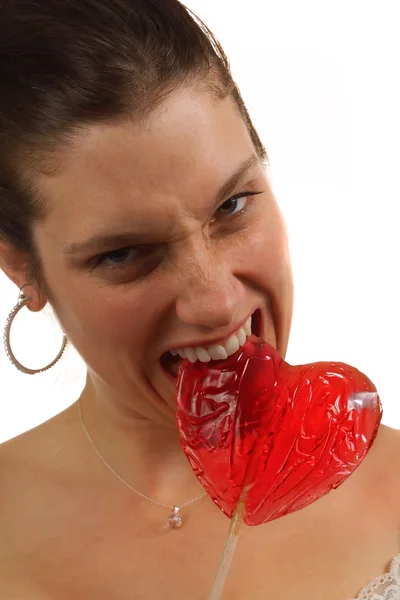 Young woman bites hard on heart shaped lollipop — Stock Photo, Image