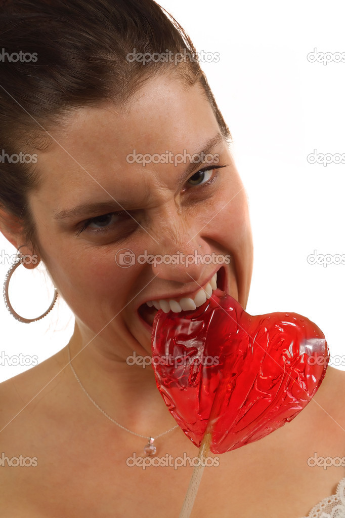 Young woman bites hard on heart shaped lollipop