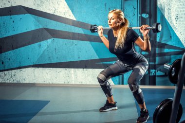 Attractive young woman doing squat exercise in modern gym. Toned image.