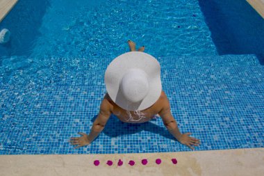 Yüzme havuzunda dinlenen şapkalı genç bir kadın.