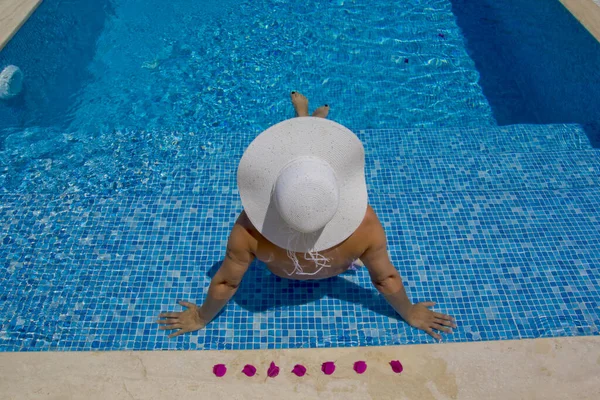 Yüzme havuzunda dinlenen şapkalı genç bir kadın.