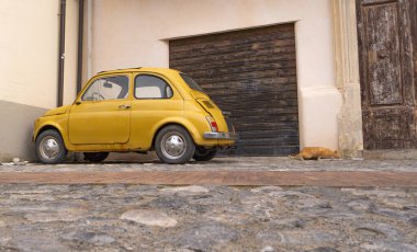 Küçük sarı bir klasik araba ve İtalya 'da bir evin önünde bir kedi.