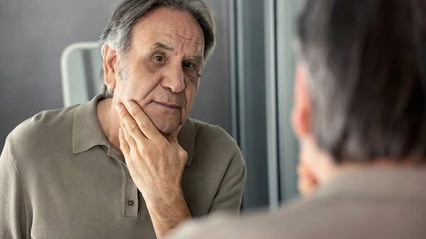 Old man looking at his face in the mirror