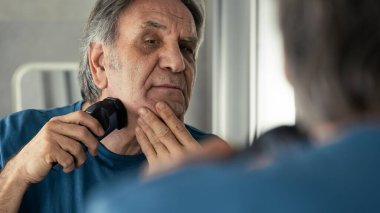 Yaşlı adam sakalını kesiyor.