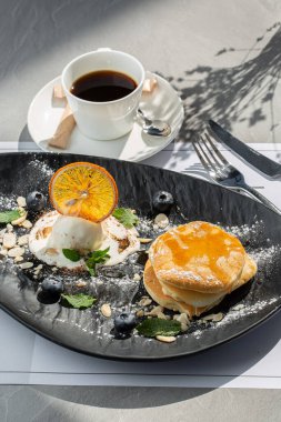 Kahveyle izole edilmiş siyah tabakta dondurmalı krep, böğürtlen ve akçaağaç pekmezi. kafe menüsü