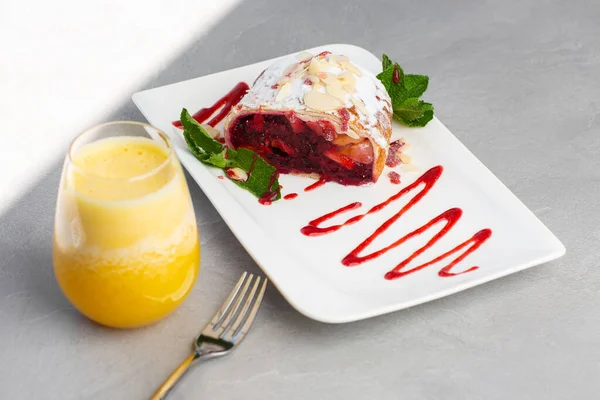 Homemade Traditional Austrian strudel with cherry or red berries and powdered sugar with glass of orange juice. Menu for cafe. Bright background.