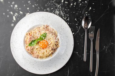 Carbonara usulü makarna. Pastırmalı spagetti, parmesan peyniri, krema sosu ve siyah mermer kaplama yumurta sarısı. Akdeniz gurme yemekleri.