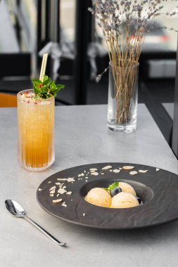 Bir tabak dondurma ve portakal kokteyli. Vanilya Dondurması Kreplerinin Kapalı Durgun Yaşamını Gri arka planda Modern Siyah Tabakta Yabanmersini ile Kapatın