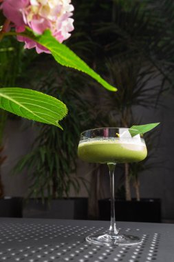 Yeşil kibrit kokteyle sahip cam arka planda yeşil yaprakla süslenmiş pembe çiçekli.