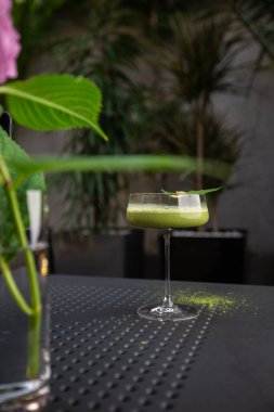 Yeşil kibrit kokteyle sahip cam arka planda yeşil yaprakla süslenmiş pembe çiçekli.