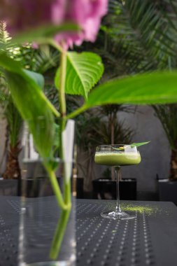 Yeşil kibrit kokteyle sahip cam arka planda yeşil yaprakla süslenmiş pembe çiçekli.