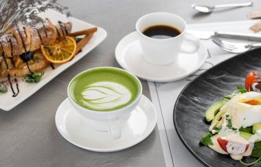Bir fincan matcha latte ve kahve. Yüksek kalite fotoğraf. Matcha, fincanda yeşil çay latte ve kruvasan. Gri arka plan. Kapatın. Üst görünüm.