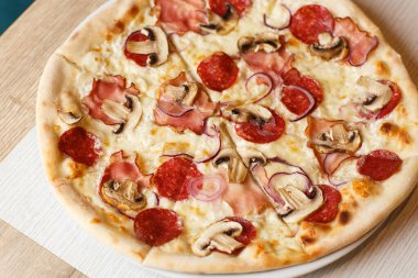 Jambonlu pizza, mantar, salam ve ahşap arka planda mozzarella yakın plan. İtalyan mutfağı. Prosciutto ve salamlı pizza, ahşap masada. en üstteki görünüm.