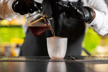 Barmen bulanık arka planda Bar sayacı üzerinde kokteyl için süzgeç aracılığıyla ölçüm cam bardak bir alkol dökme