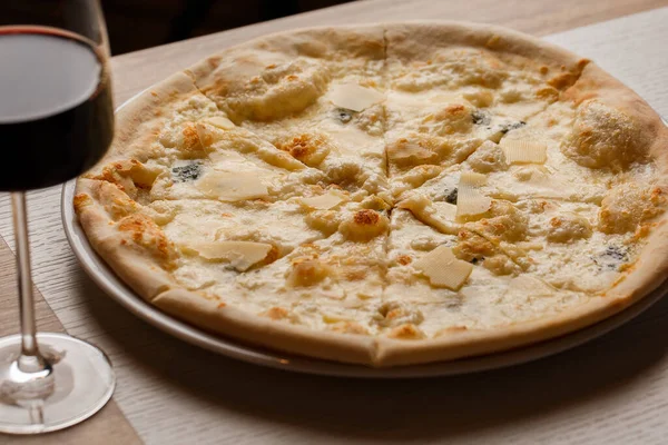 Cztery ser pizza quattro formaggi ze szklanką wina na ciemnym tle. — Zdjęcie stockowe